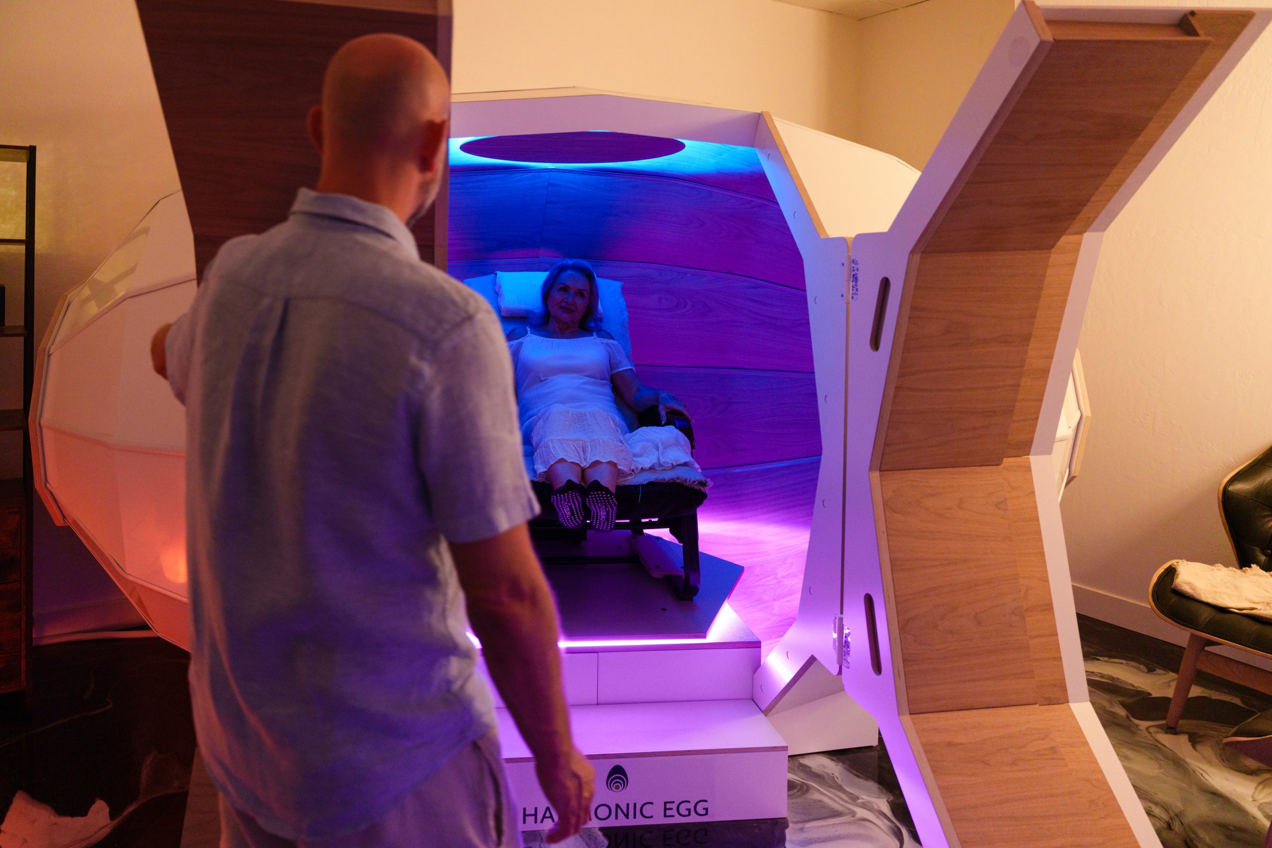 A woman relaxing inside the Harmonic Egg light and sound therapy chamber at Tinted Salt Wellness in Chandler, Arizona.